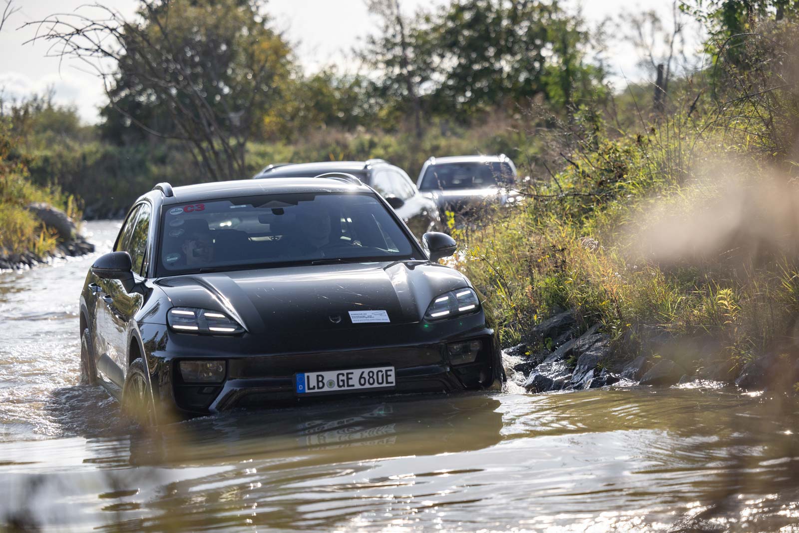 A line of Porsche Macans going through a body of water up to the license plate