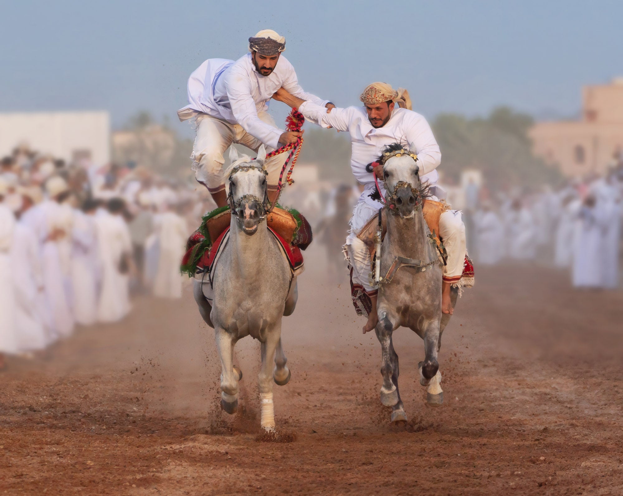 Two horses running with riders holding each other's arms