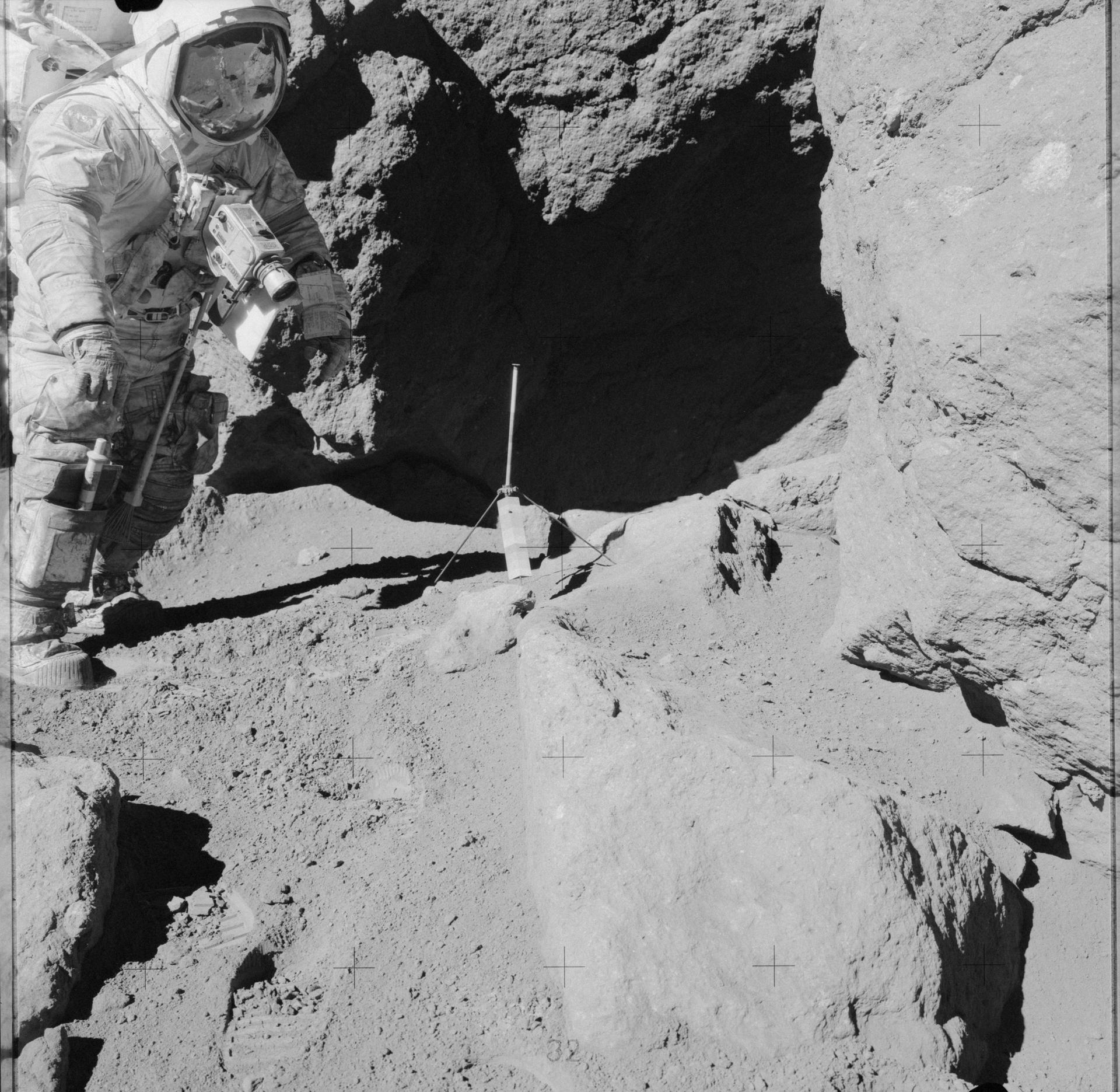 An astronaut with a camera on his chest stands amongst boulders