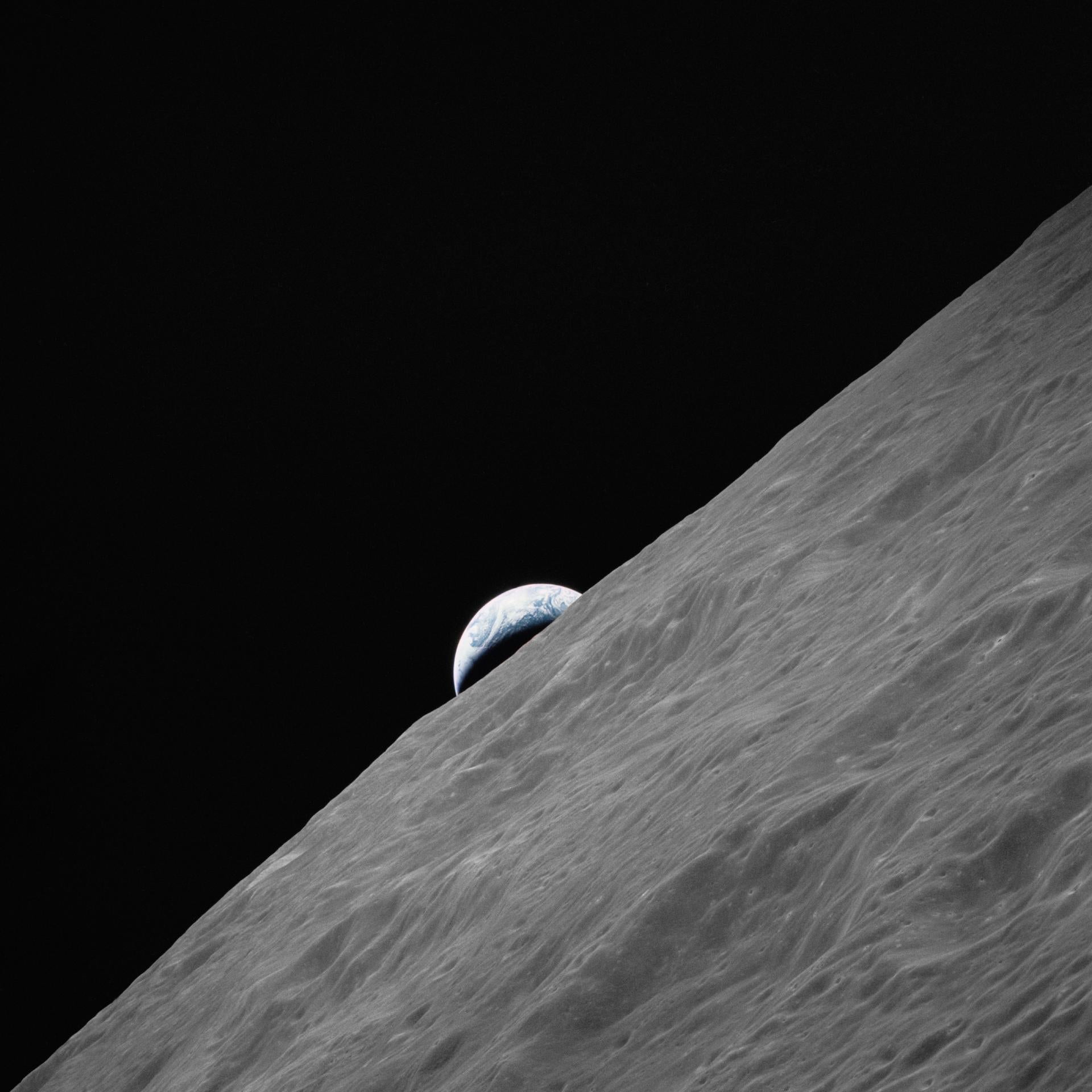 the grey surface of the moon in the foreground with earth in the background