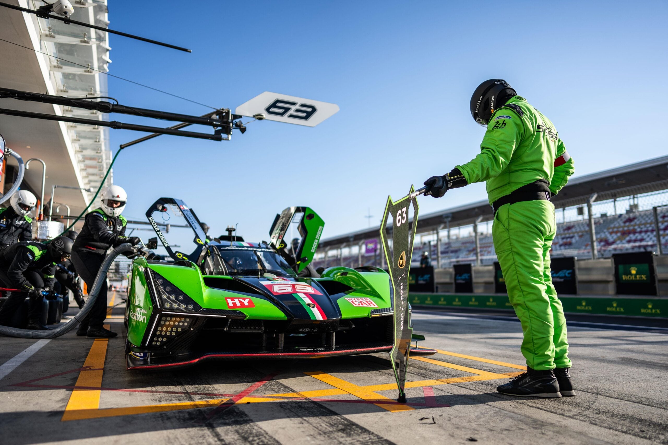 a man in a green suit stands in front of a green, red, and black race car on a rack track