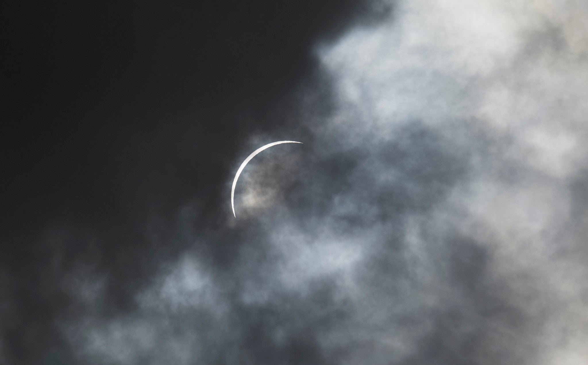 a sliver of the sun remains as moon and clouds move over it