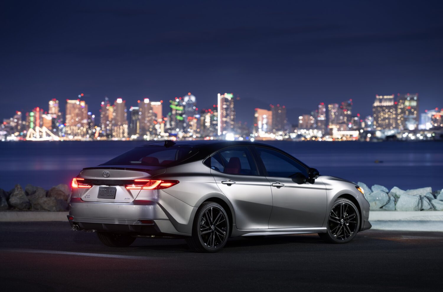 grey sedan at night in front of city skyline