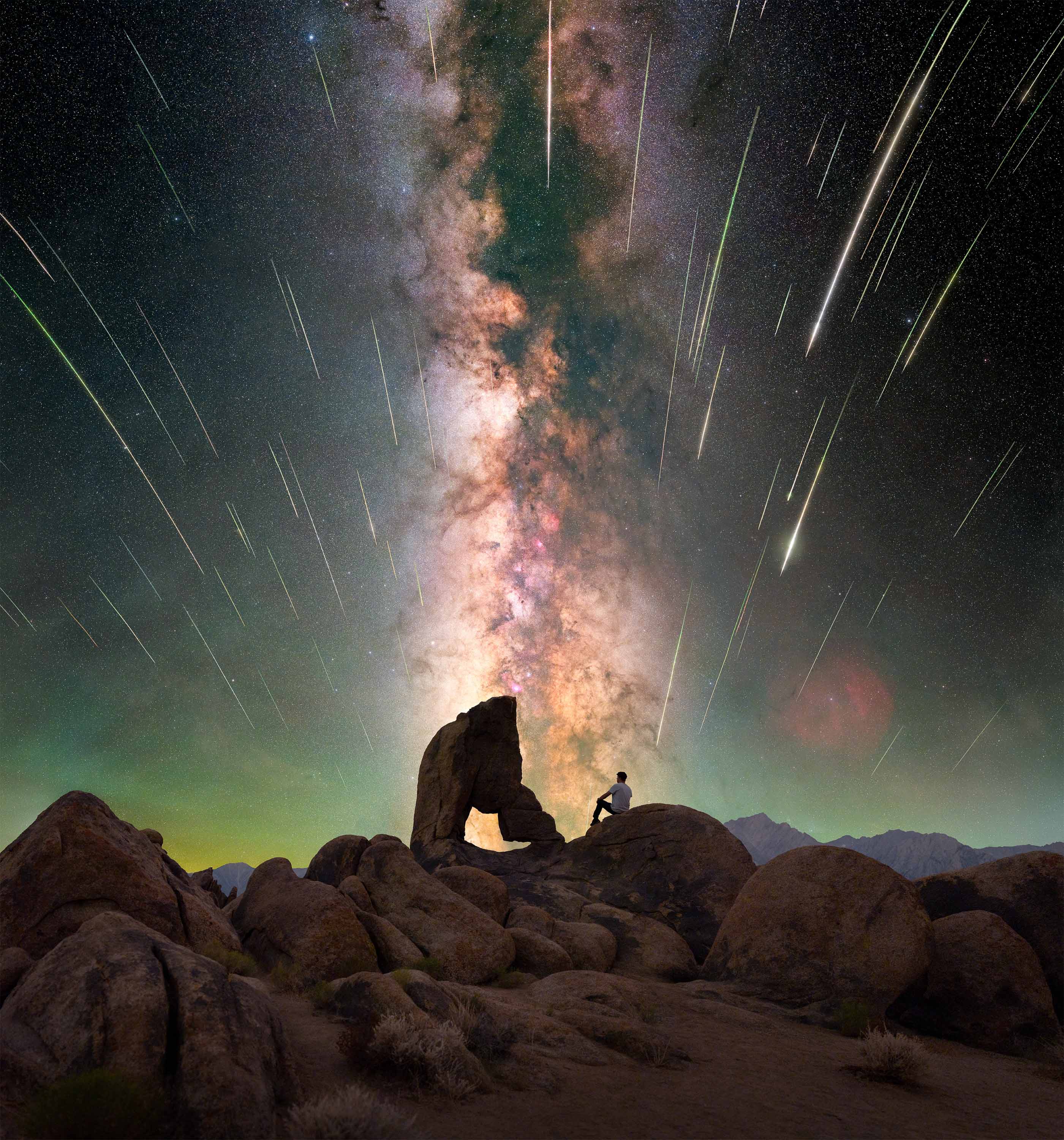 man sitting on large boulder. milky way and shooting stars in the sky