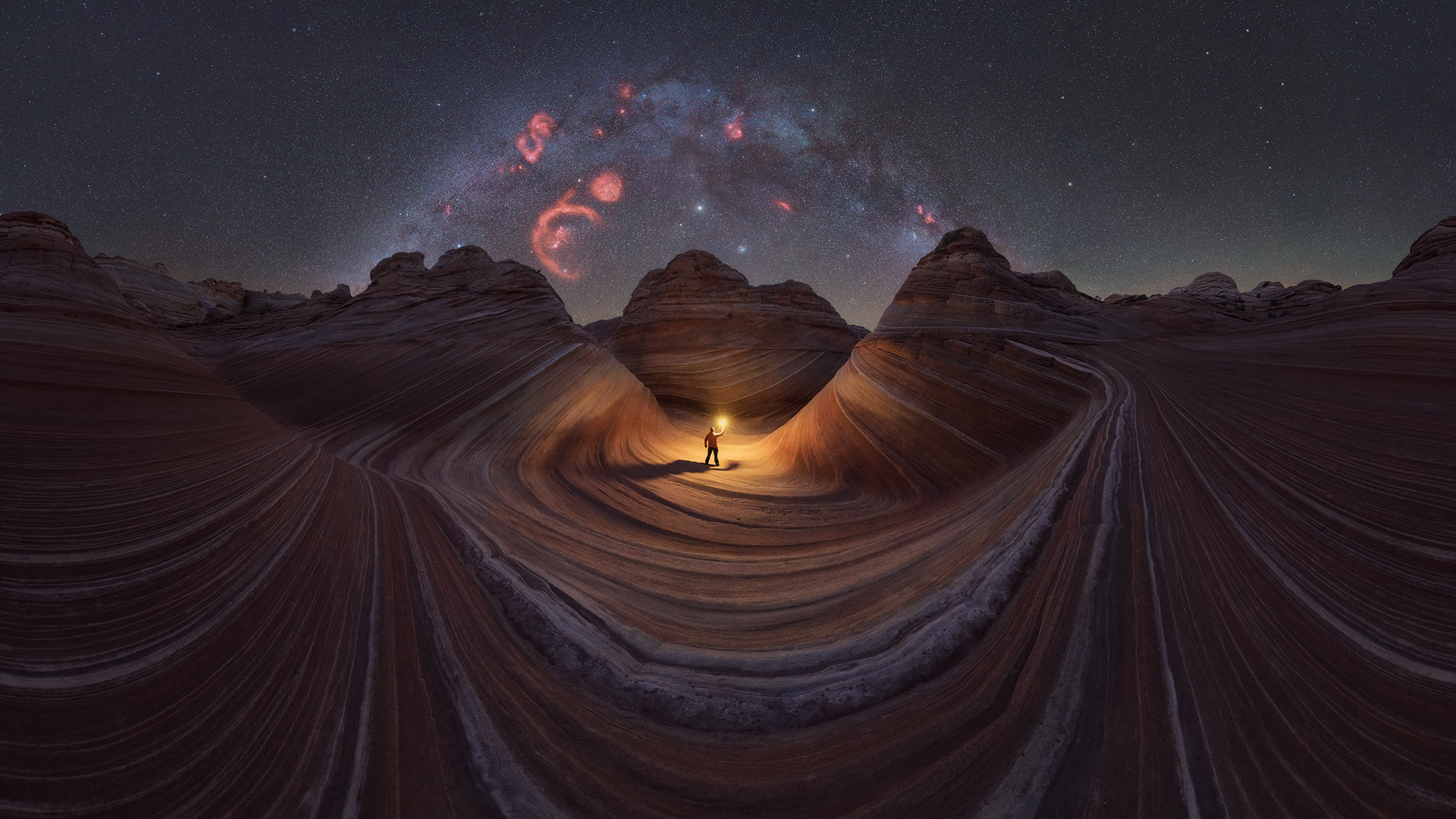 person holding a light in striped sandstones with milky way above