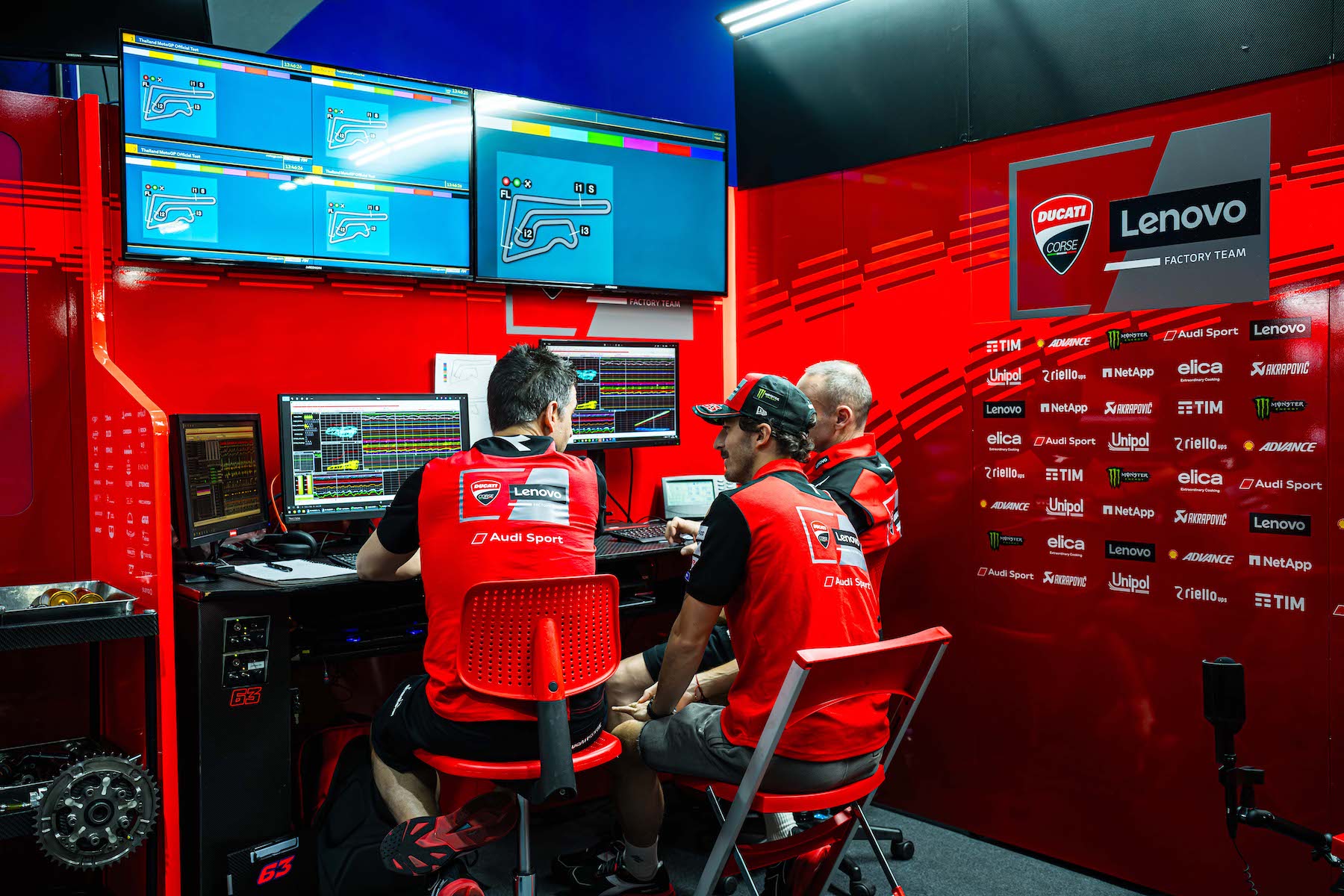 three men sit in chairs looking at multiple computer screens