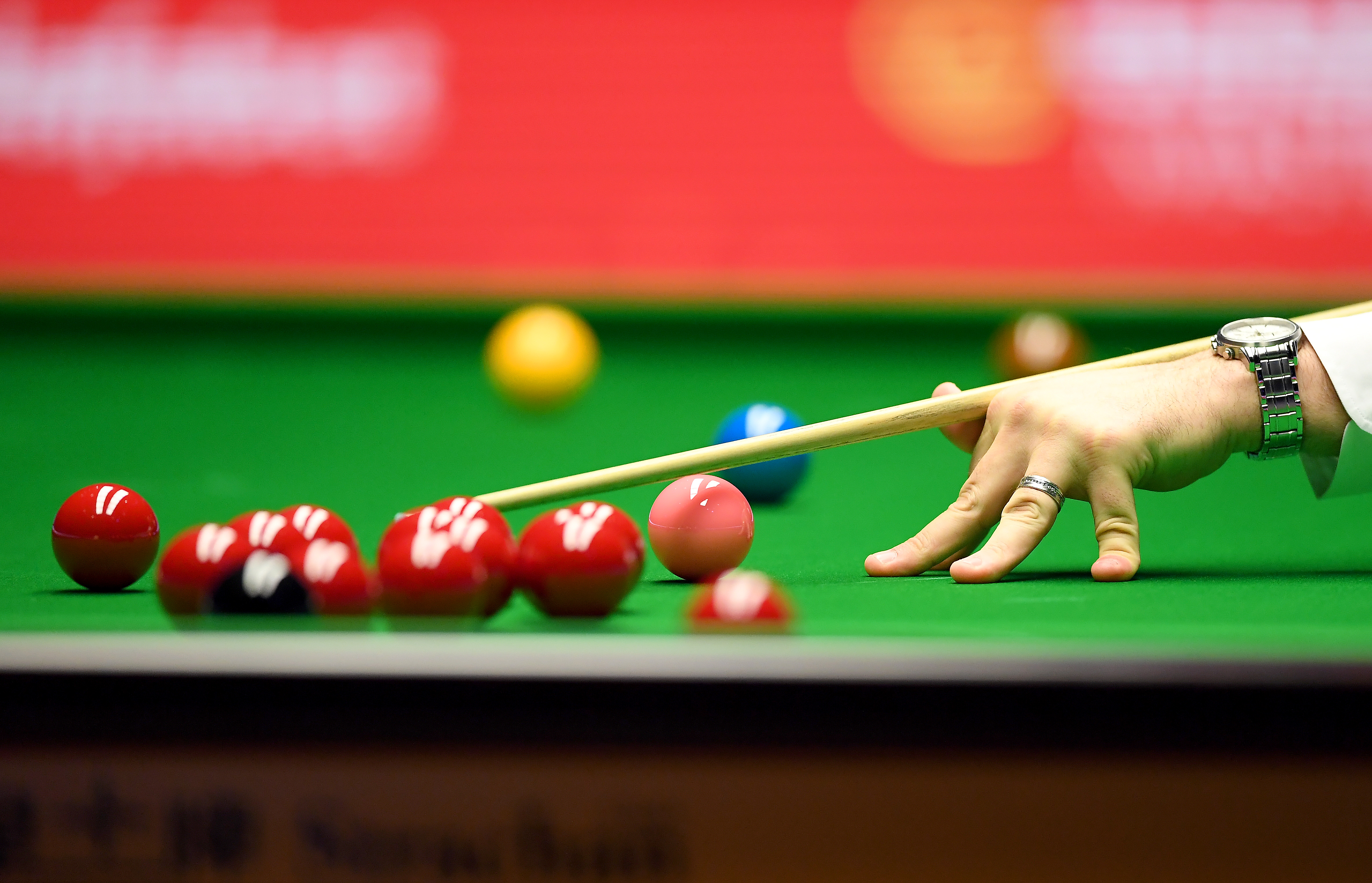 a detailed view of a person holding a cue and going in to break snooker balls. most of the balls are red, with one pink, one blue, and one yellow