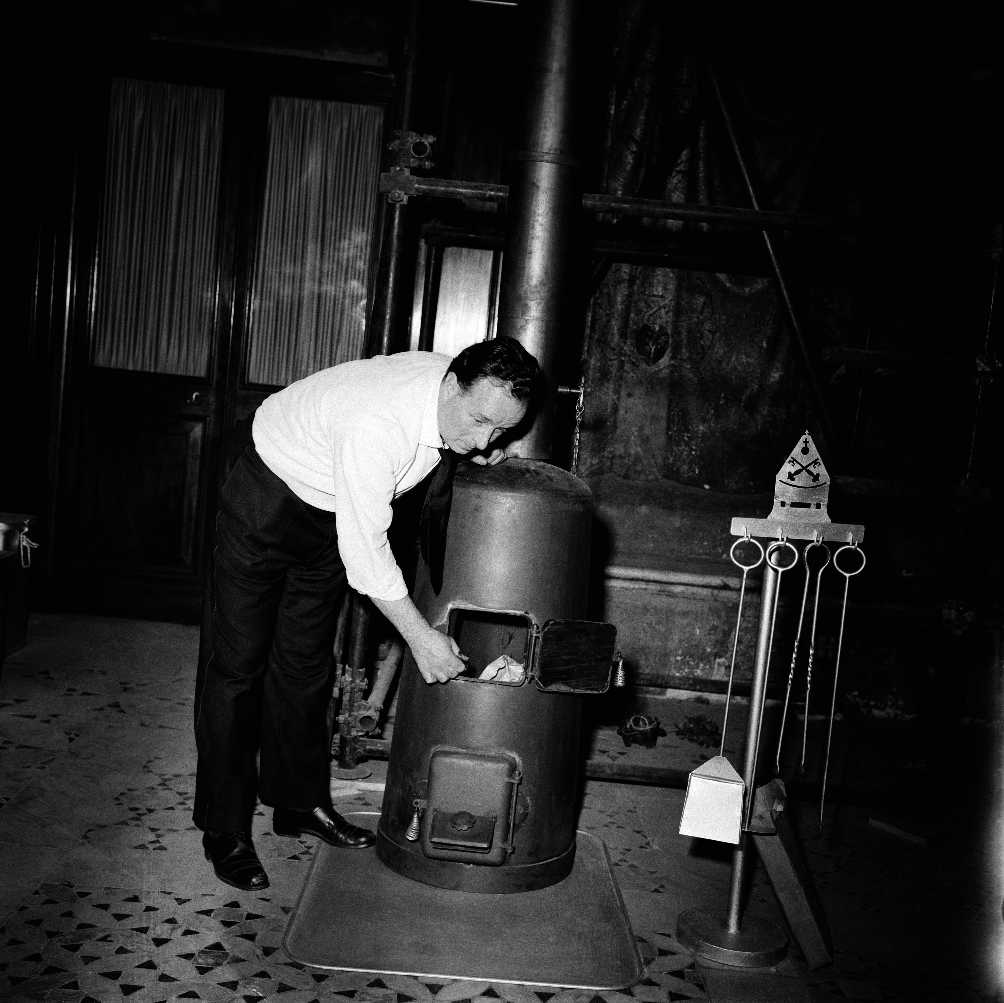 a black and white photo of a man placing crumpled up ballots into a furnace