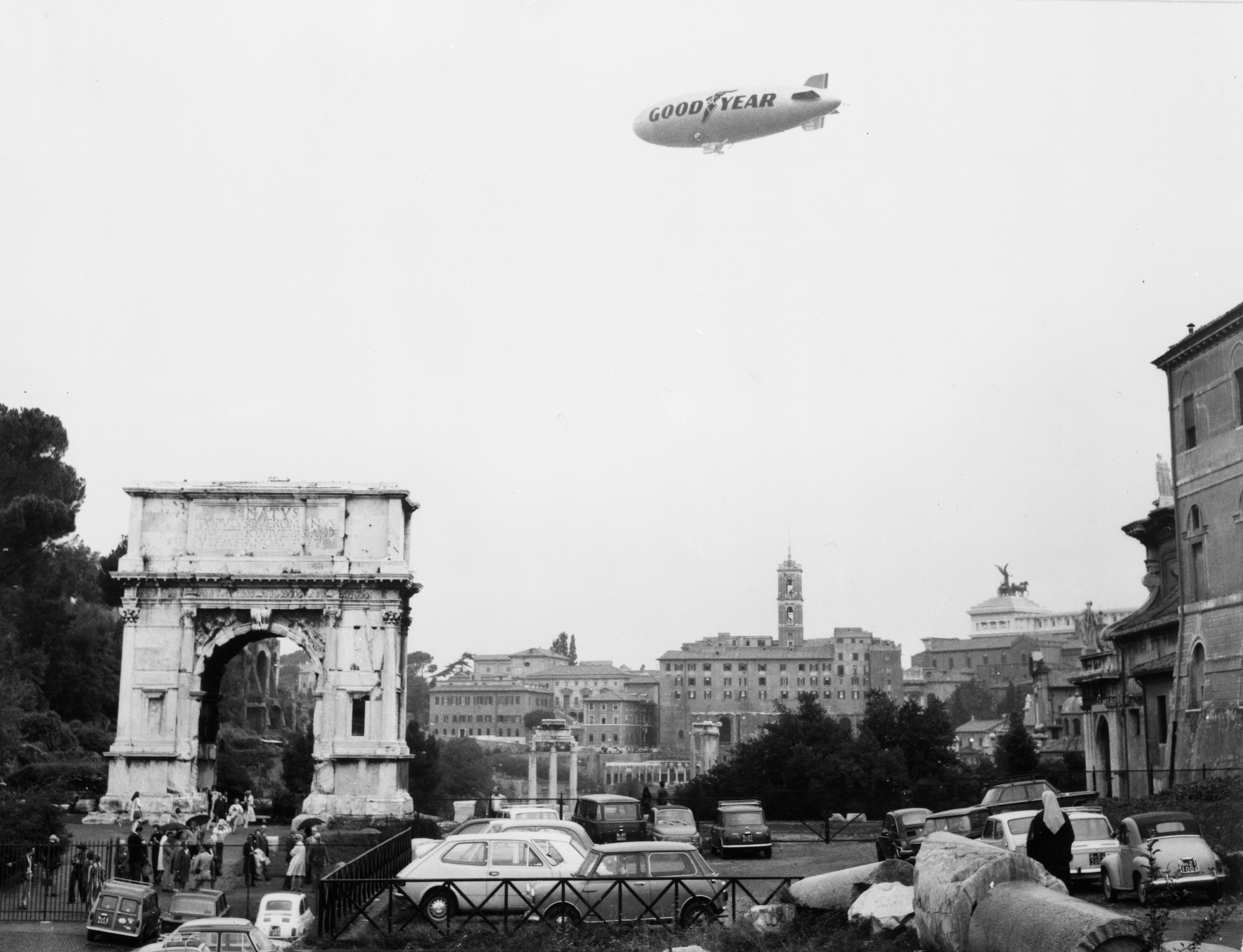 blimp flyin over rome. a nun looks on