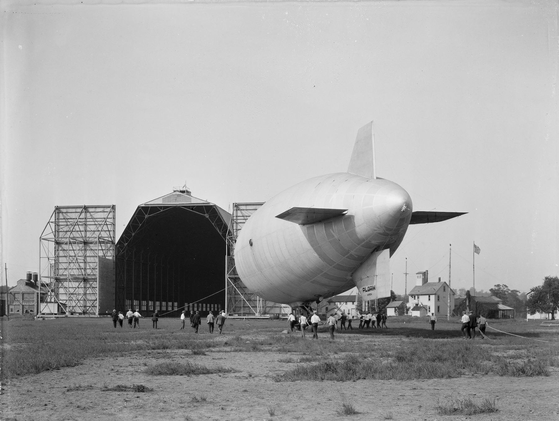 an unmarked blimp is move to a hanger as people hold ropes