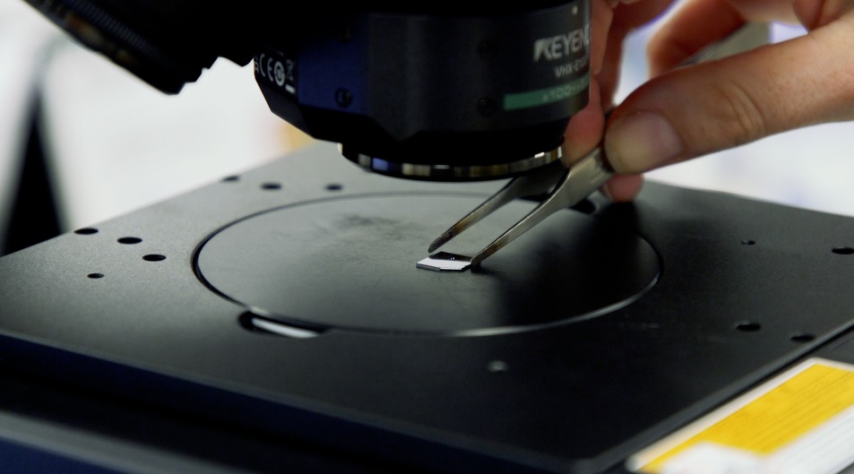 Glass slide being placed under microscope with tweezers