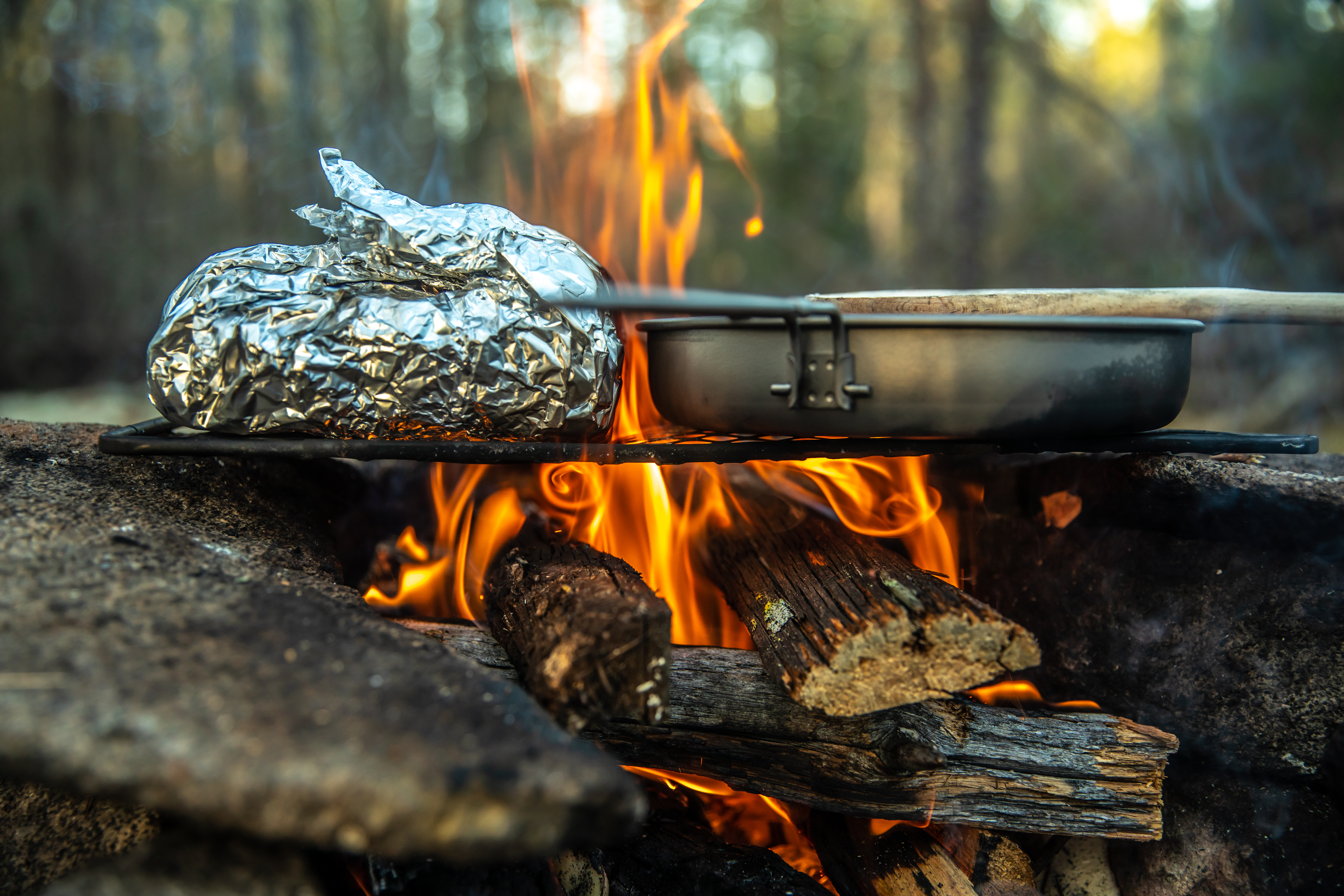 a campfire with a baked potato in tin foil, next for a frying pan