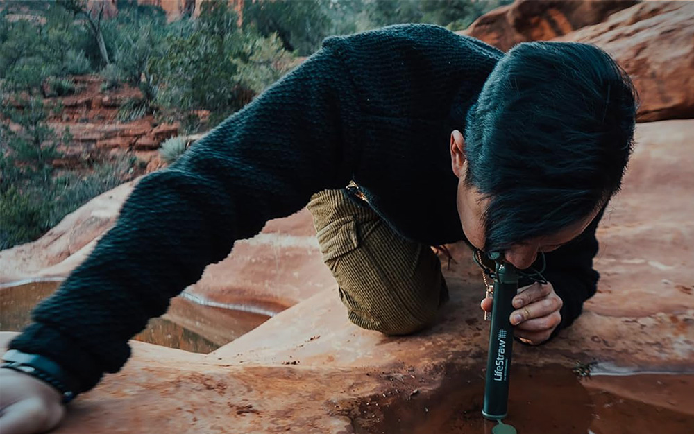  Person drinking water out of a puddle through a LifeStraw personal water filter