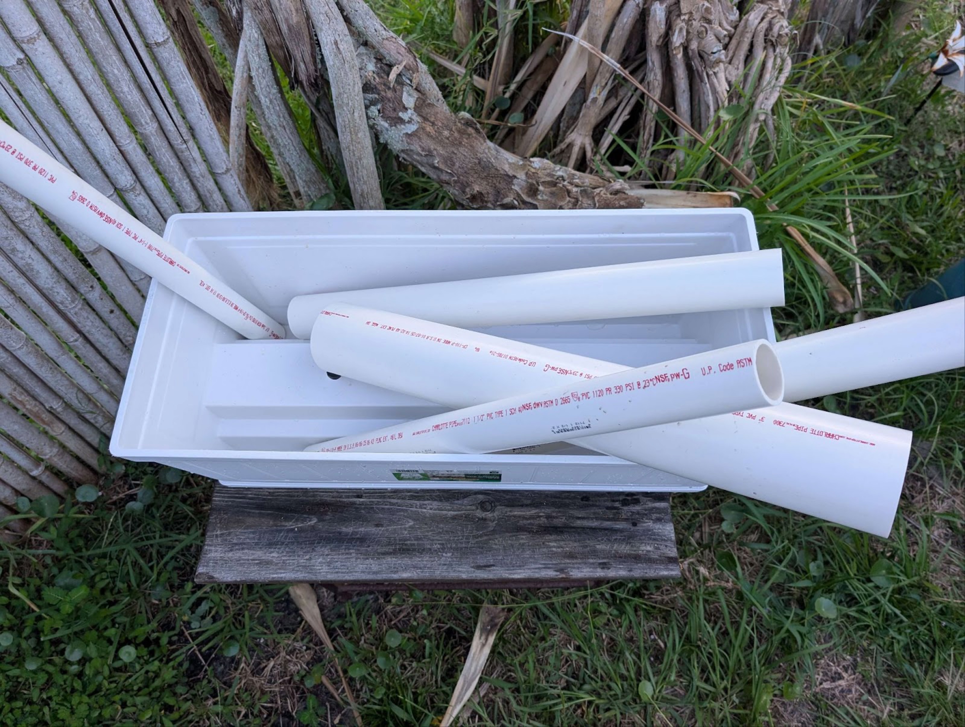 planter and PVC pipes on a wood bench in grassy area