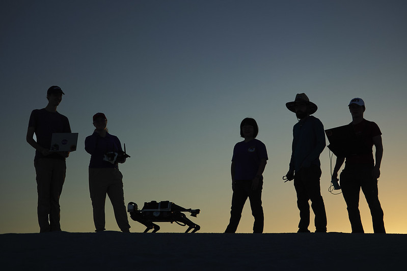 a silhouette of five scientists and their quadruped robot as the sun sets on White Sands National Park