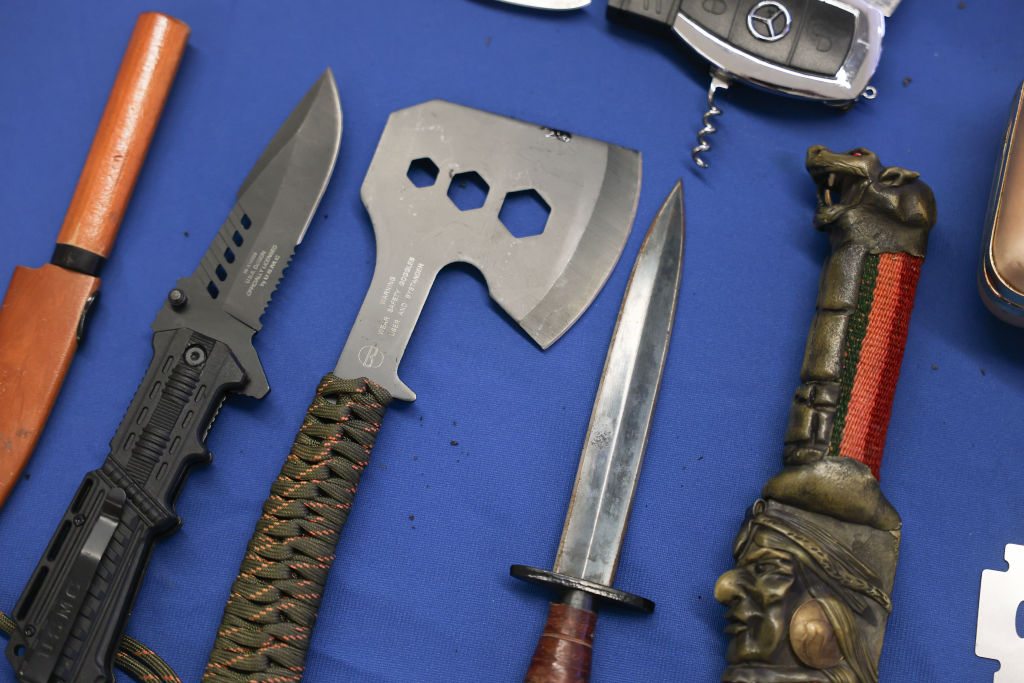 Three knives, a camping axe, a knife hilt designed to look like a bat, and a BMW car key multitool are laid out on a blue surface.