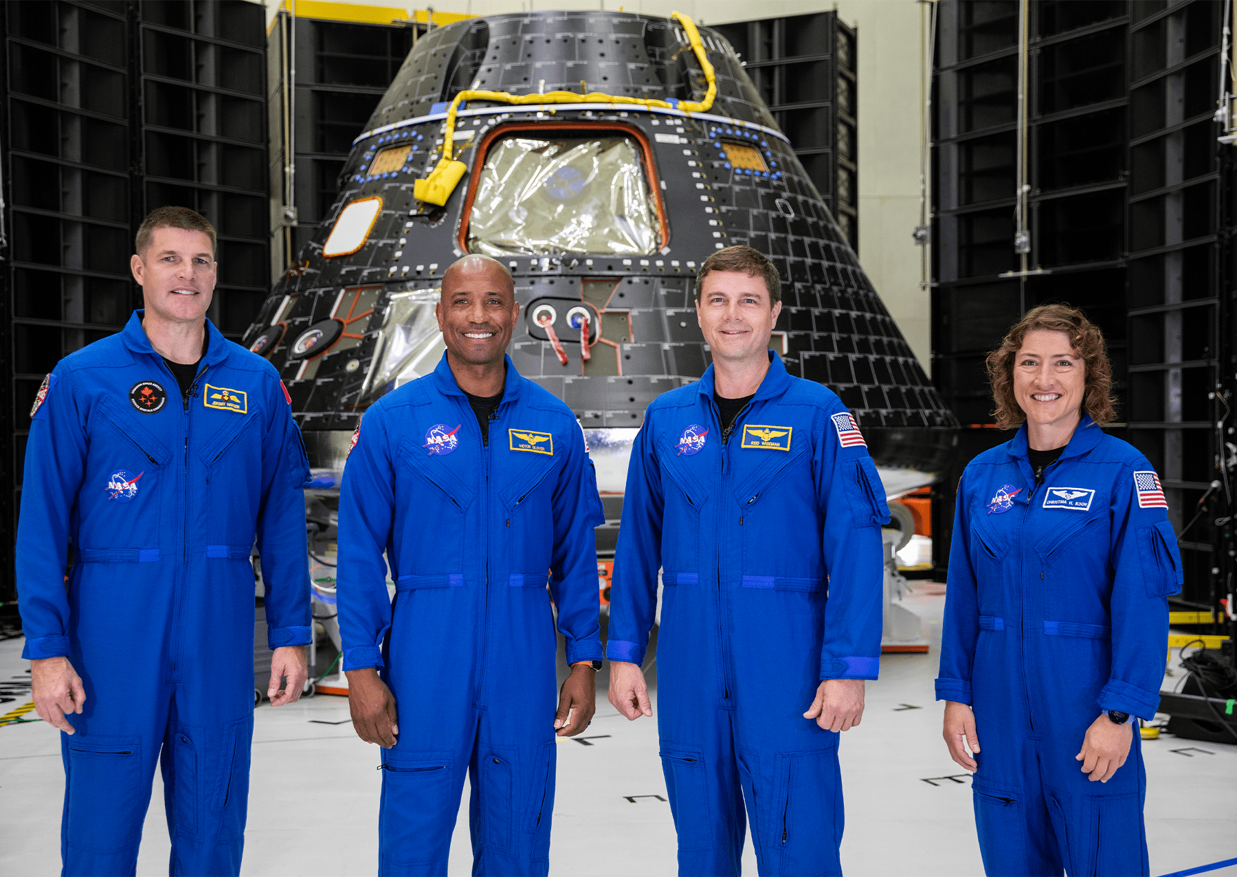 four memebers of the artemis 2 crew stand in a linke in blue jumpsuits. from left: Jeremy Hansen, mission specialist; Victor Glover, pilot; Reid Wiseman, commander; and Christina Hammock Koch, mission specialist.