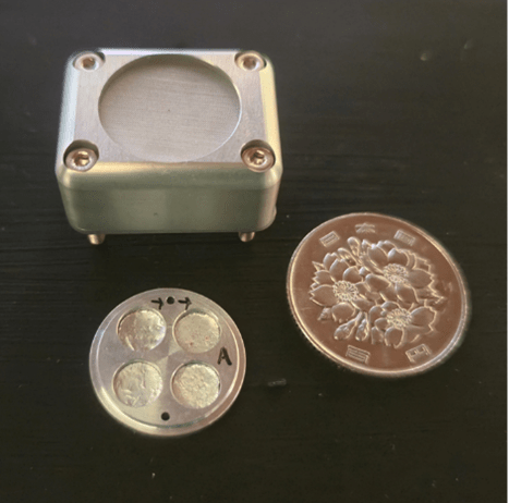 The space exposure unit used for the experiment next to a 100-yen coin for scale.