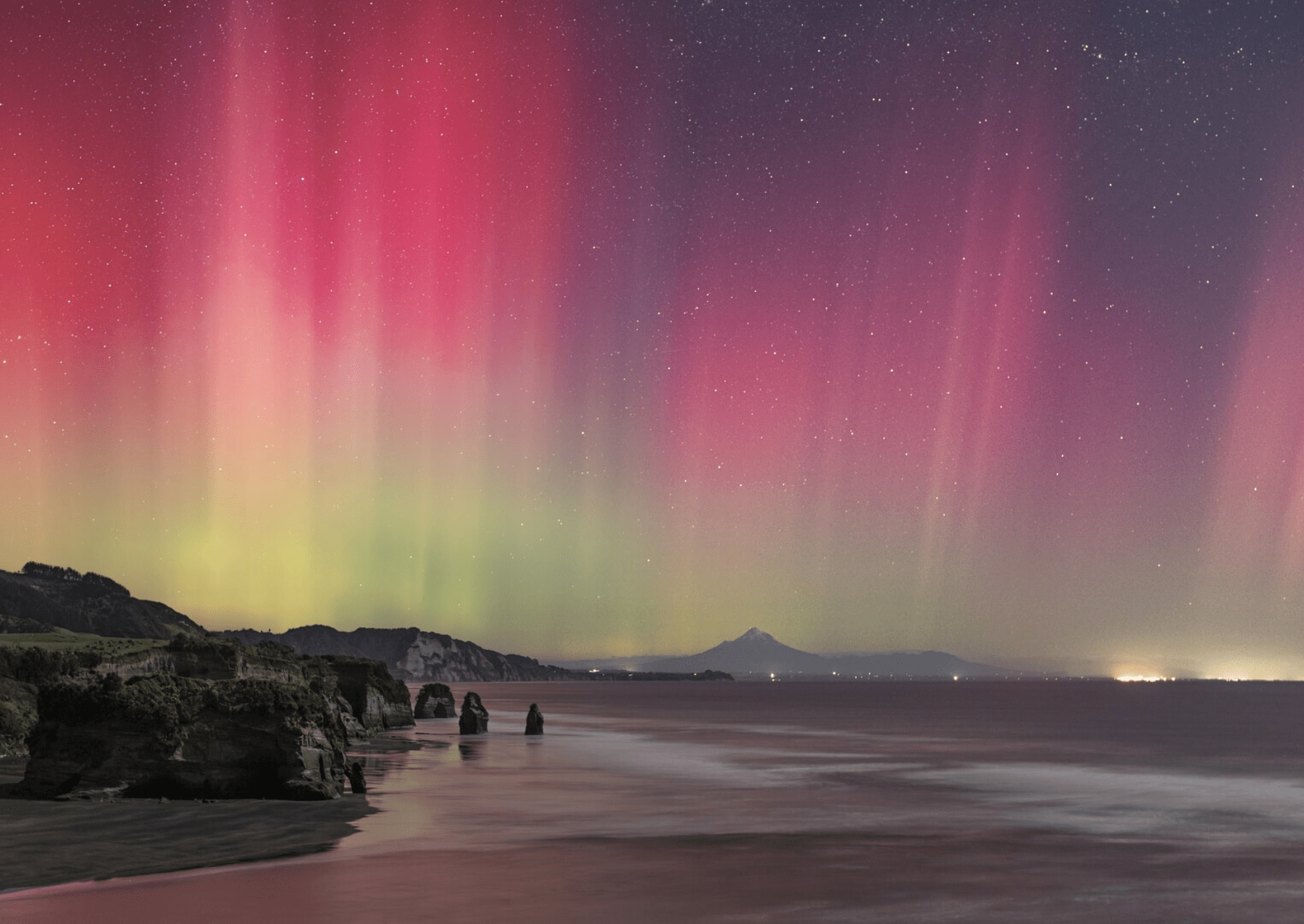 a pink and yellow aurora glows over a beach with large standing stones