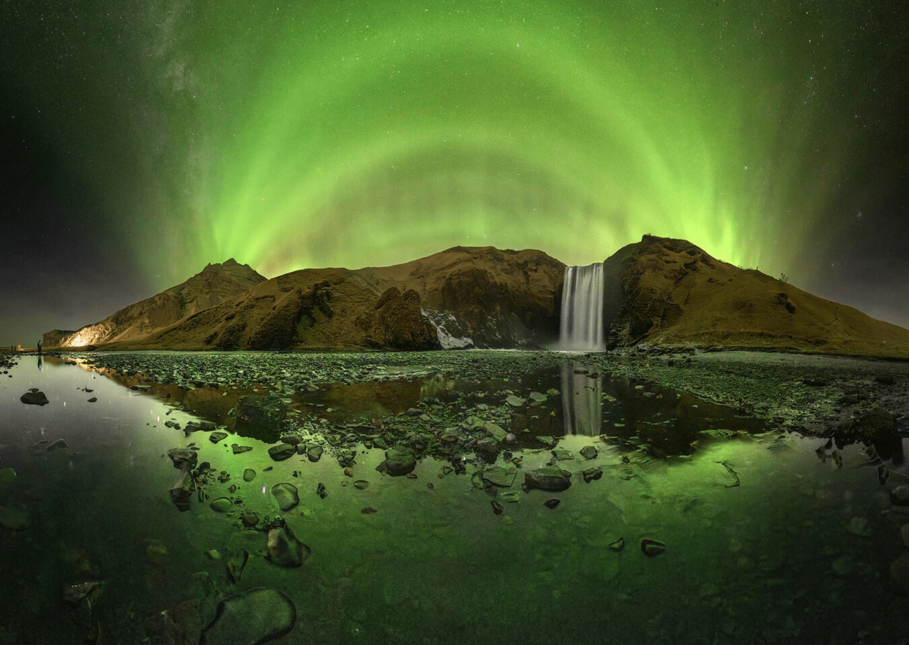 a bright green aurora over a waterfall and reflecting in a stony pool