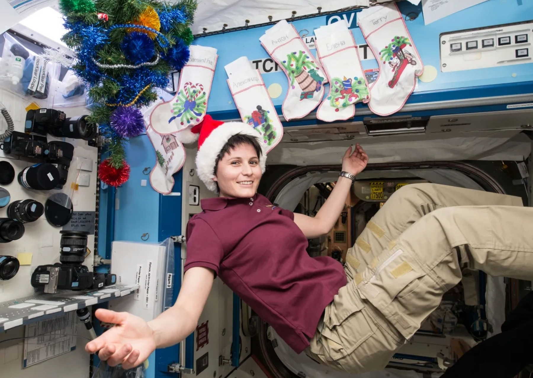 a female astronaut poses with a santa hat on and floating