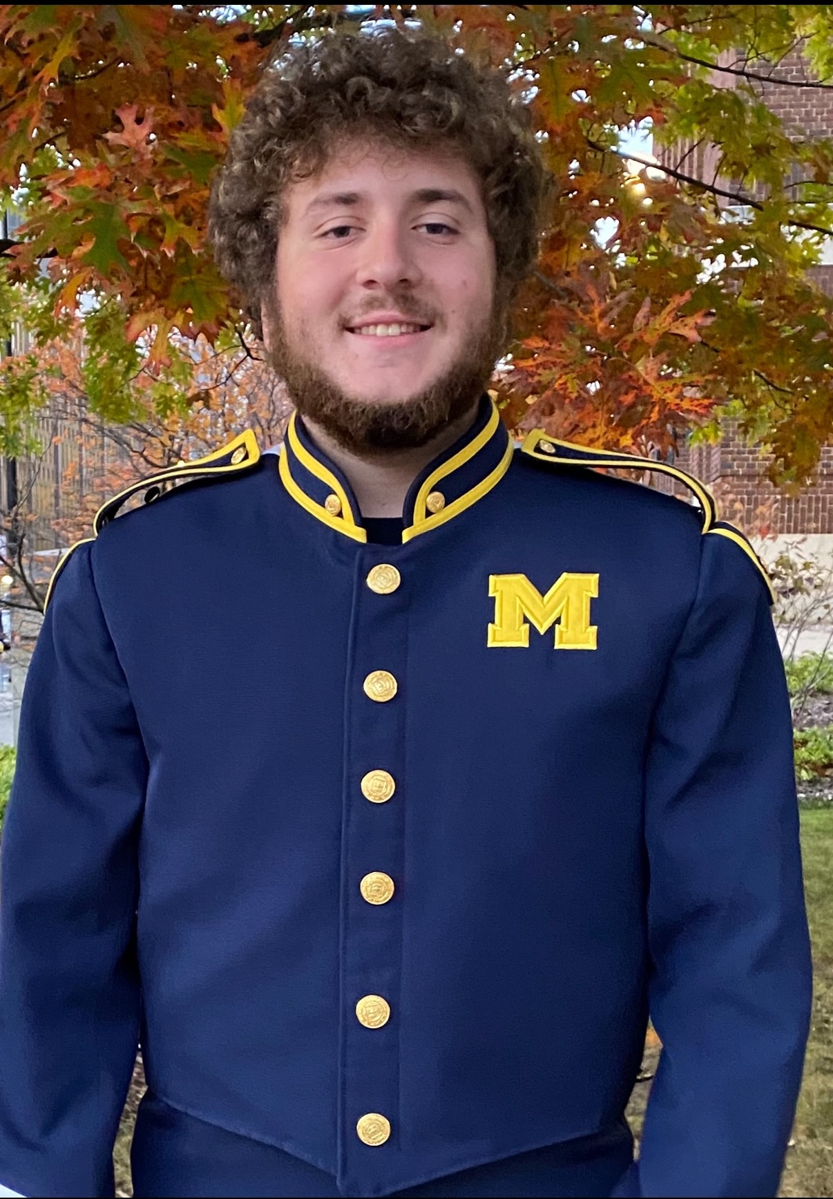 a man in a blue marching band uniform with a bright yellow letter m on the left chest