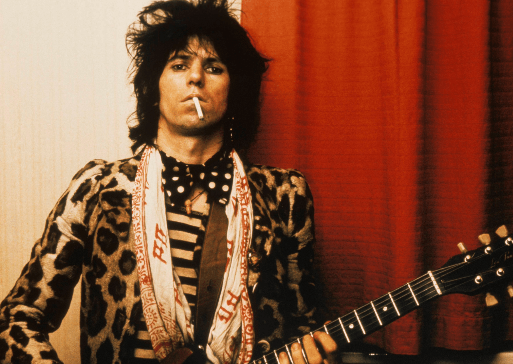 musician keith richards holding a guitar with a cigarette in his mouth