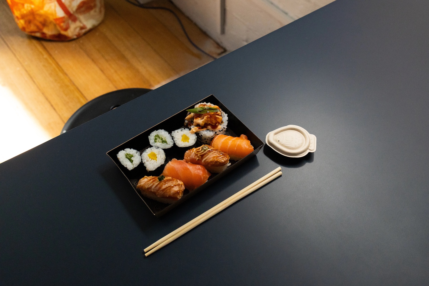 a plate of sushi on a black tables, with chopsticks and a fish-shaped soy sauce continer