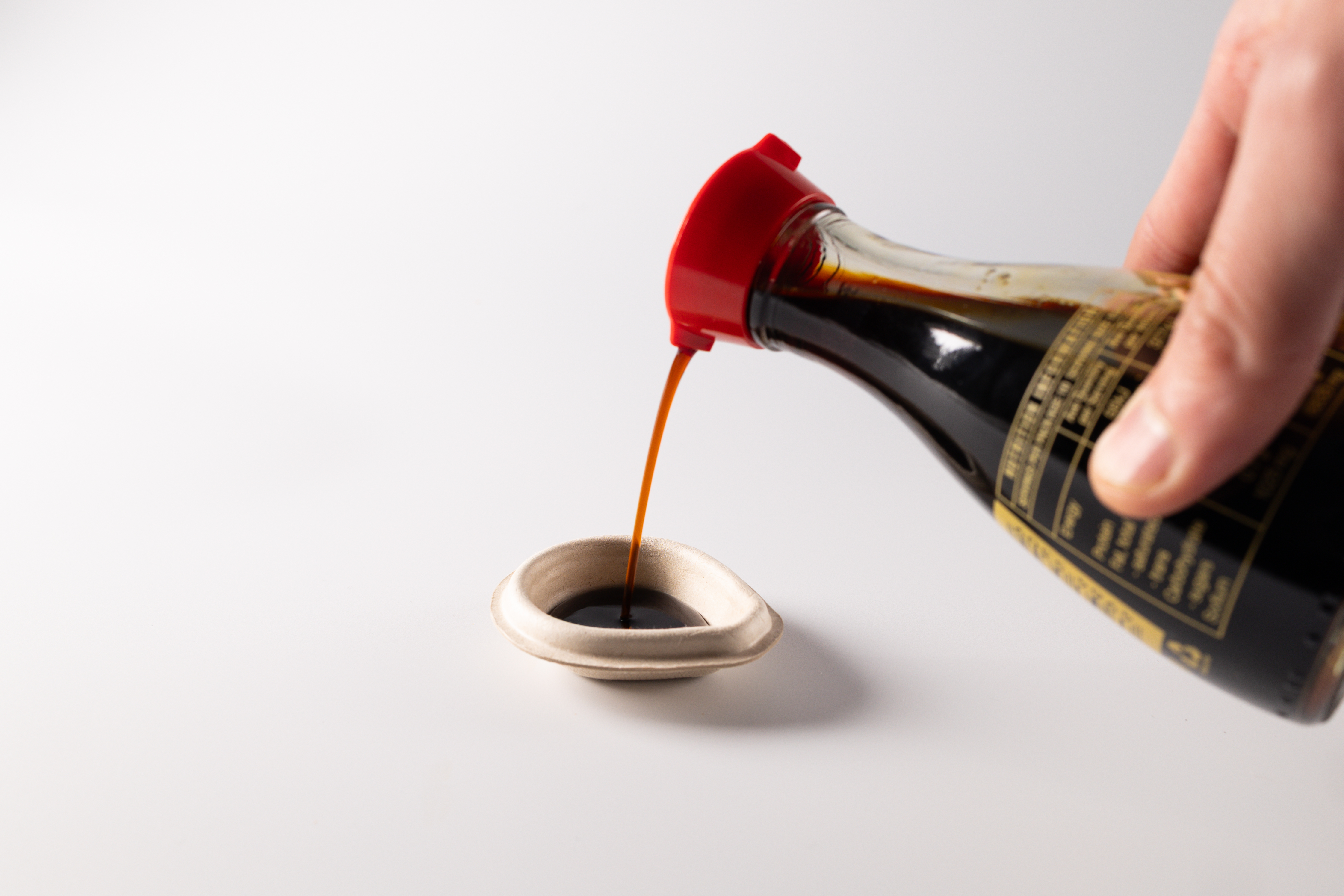 a hand pouring brown soy sauce into a container
