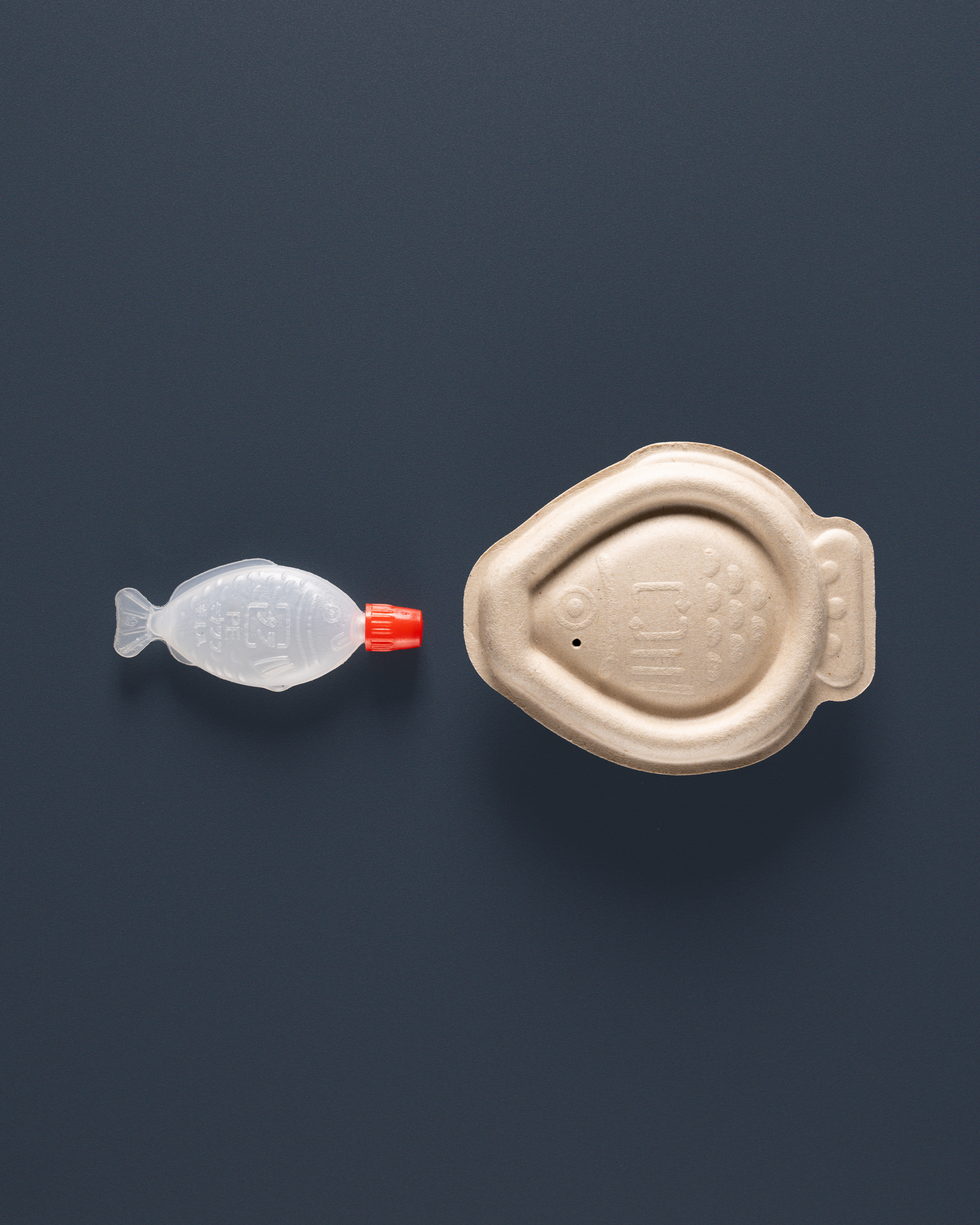 A traditional plastic fish-shaped soy sauce container (left) with the new biodegradable option (right).
